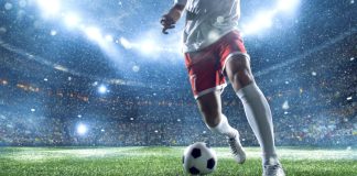 Jogador driblando uma bola num campo de futebol.