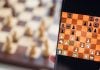 Foto de celular com jogo de xadrez on-line, com tabuleiro desfocado atrás