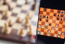 Foto de celular com jogo de xadrez on-line, com tabuleiro desfocado atrás