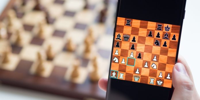 Foto de celular com jogo de xadrez on-line, com tabuleiro desfocado atrás