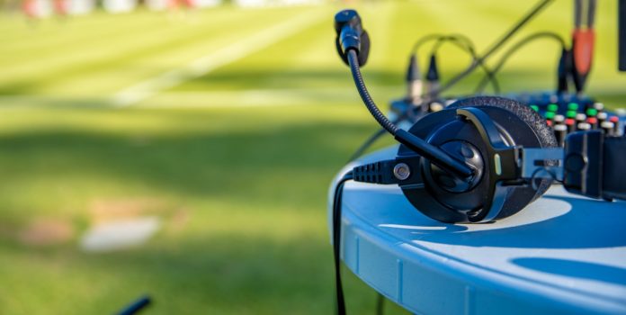 multibet-parceria-ale-oliveira-radio-itatiaia Fones de ouvido de comentaristas sobre a mesa ao lado do campo de futebol