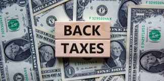 Governo avalia aplicar cobrança retroativa a empresas de apostas Back Taxes escrito em blocos de madeira, posicionados sobre notas de dólares