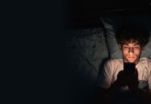Rapaz mexendo no celular no escuro deitado na cama
