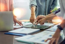 Grupo de pessoas discutindo projetos com papéis e iPad sobre a mesa