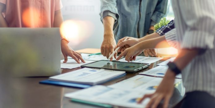 Grupo de pessoas discutindo projetos com papéis e iPad sobre a mesa