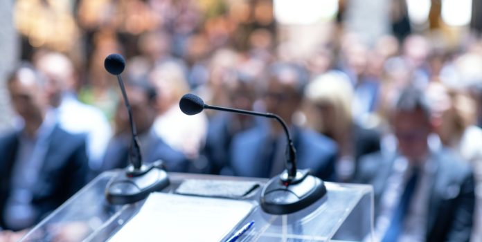 encontro-nacional-combate-manipulação-apostas-esportivas Microfone de uma sala de conferência com pessoas desfocadas no fundo