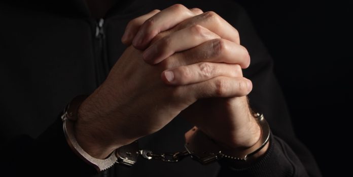 Homem sentado algemado com as mãos cruzadas
