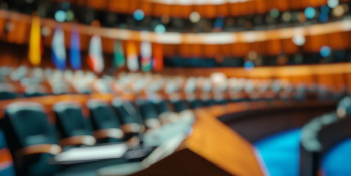 Sala de conferência com pódio e assentos vazios para debates políticos