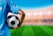 Homem segurando bola de futebol vestindo camiseta 7 em frente ao campo
