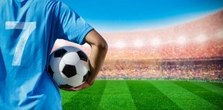 EstrelaBet patrocina Kings Cup Brazil no CazéTV Homem segurando bola de futebol vestindo camiseta 7 em frente ao campo