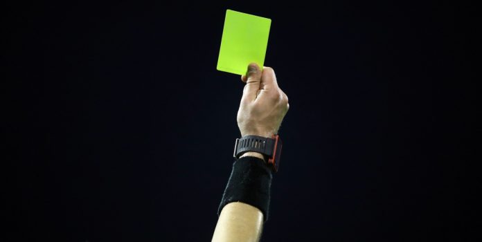 Mão de juíz de futebol segurando cartão amarelo