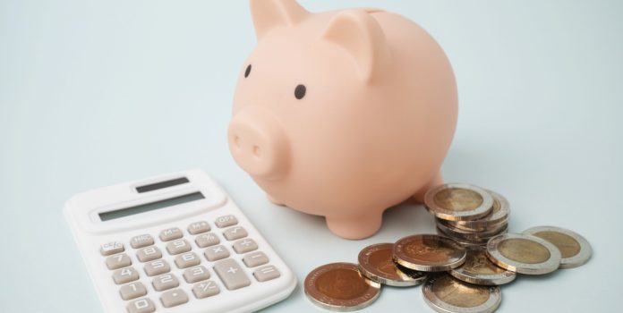 Cofre de dinheiro em formato de porco, calculadora e moedas sobre a mesa