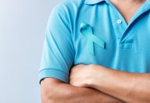 Homem com os braços cruzados vestindo camiseta azul com o símbolo do Novembro Azul