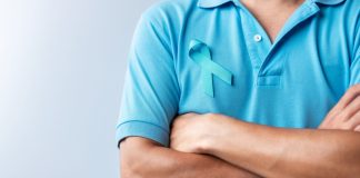 Homem com os braços cruzados vestindo camiseta azul com o símbolo do Novembro Azul