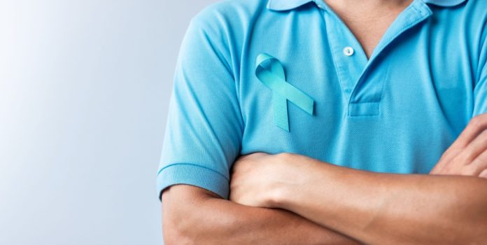 Homem com os braços cruzados vestindo camiseta azul com o símbolo do Novembro Azul