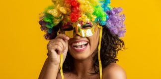 Mulher sorrindo segurando máscara e com peruca de cabelo de carnaval
