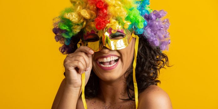 esportes-da-sorte-renova-parceria-com-pre-caju-2025 Mulher sorrindo segurando máscara e com peruca de cabelo de carnaval