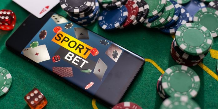 novos-pls-de-combate-à-ludopatia-e-restrição-de-apostas- Fichas de cassino e celular com a tela apresentando "apostas esportivas" em inglês sobre a mesa de jogo