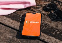 Smartphone sobre o chão com o logo da Betano na tela, com óculos de sol e bolsa ao lado dele