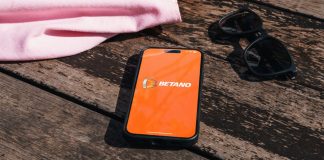 Blask e brmkt.co revelam ranking das maiores casas de apostas do Brasil Smartphone sobre o chão com o logo da Betano na tela, com óculos de sol e bolsa ao lado dele