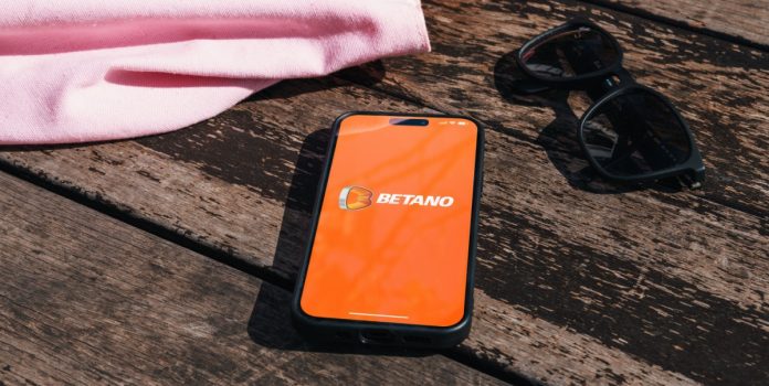 Blask-e-brmkr.co-revelam-ranking-das-maiores-casas-de-apostas-do-Brasil Smartphone sobre o chão com o logo da Betano na tela, com óculos de sol e bolsa ao lado dele