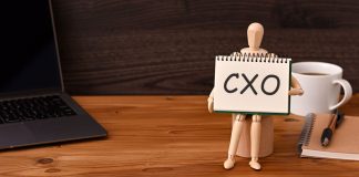 EstrelaBet apresenta Lorena Lima como diretora de Experiência do Cliente e Expansão Boneco segurando cartaz com a sigla CXO sobre a mesa, ao lado do notebook. da xícara de café e do bloco de notas