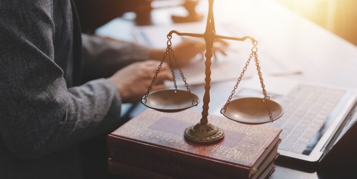 SPA-reforça-exigências-administrativas-para-operadores-de-apostas Homem sentado em escritório, com papéis sobre a mesa e a balança representando a advocacia