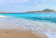 Nova campanha da BETesporte reforça conexão com brasileiros Mar calmo e faixa de areia em dia ensolarado com montanhas atrás