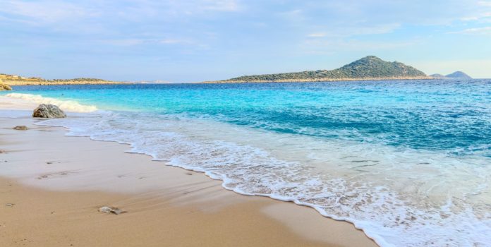 betesporte-lança-campanha-com-zico-e-vampeta Mar calmo e faixa de areia em dia ensolarado com montanhas atrás