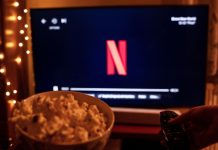 Os Donos do Jogo: bastidores da indústria ilegal do jogo do bicho Balde de pipoca e televisão ligada com o símbolo da Netflix em uma sala com pouca luz