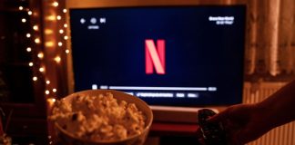 Os Donos do Jogo: bastidores da indústria ilegal do jogo do bicho Balde de pipoca e televisão ligada com o símbolo da Netflix em uma sala com pouca luz
