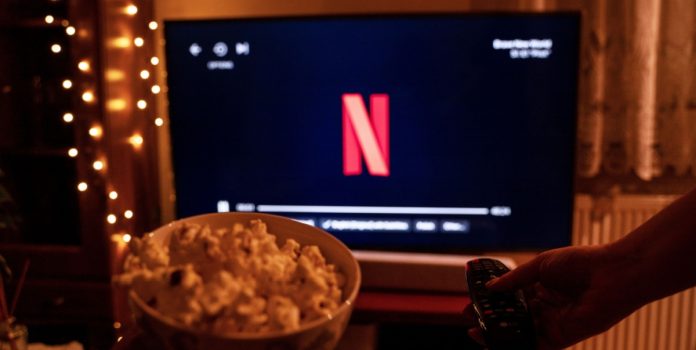 Balde de pipoca e televisão ligada com o símbolo da Netflix em uma sala com pouca luz