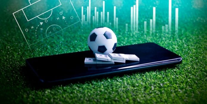 Uma bola de futebol e maços de dinheiro sob um smartphone, simbolizando apostas esportivas.