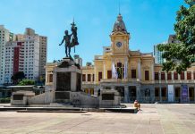 Belo Horizonte cria política para prevenir e tratar ludopatia Foto tirada de uma praça em Belo Horizonte, onde é possível ver uma estátua ao centro e uma igreja ao fundo.