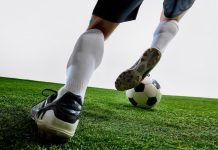 Foto tirada das pernas de um jogador de futebol driblando com a bola.