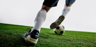 Foto tirada das pernas de um jogador de futebol driblando com a bola.