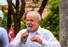Presidente Lula, um homem branco de idade avançada e cabelos brancos, discursa com um microfone em mãos.
