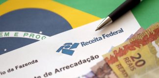 Uma folha da Receita Federal com notas de 20, 10 e 5 reais apoiada na bandeira do Brasil.