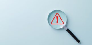 Lupa com foco em símbolo vermelho de alerta com fundo azul