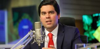 Foto tirada de André Fufuca, um homem branco de meia idade em frente a um microfone, líder do Ministério do Esporte.