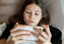 Brasil avalia implementar verificação de faixa etária em lojas de aplicativos e plataformas digitais Menina deitada na cama mexendo no celular