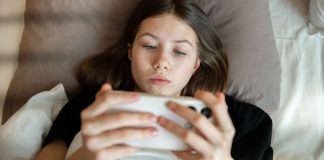 Brasil avalia implementar verificação de faixa etária em lojas de aplicativos e plataformas digitais Menina deitada na cama mexendo no celular