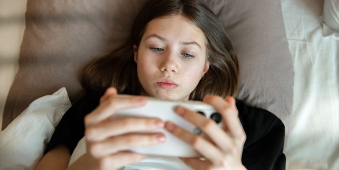 Brasil-avalia-implementar-verificação-de-faixa-etária-em-lojas-de-aplicativos-e-plataformas-digitais Menina deitada na cama mexendo no celular