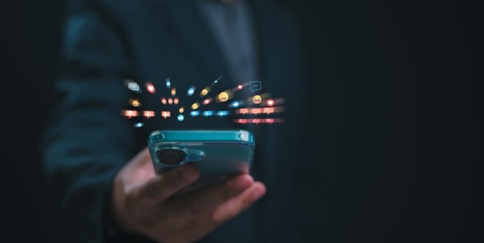 Pessoa segurando um smartphone com uma série de emojis saindo da tela.