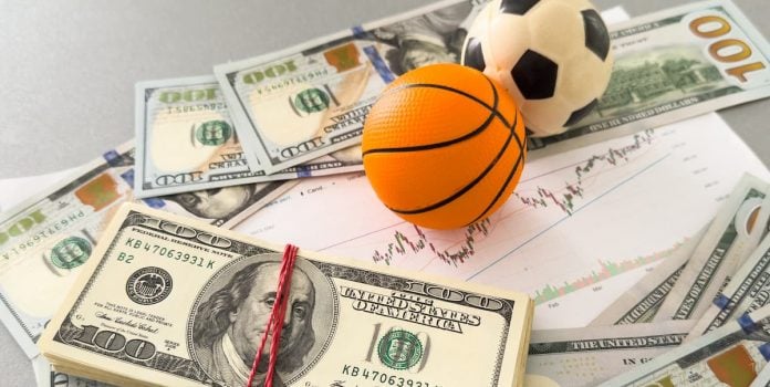 Bolas de basquete e futebol sob maços de dinheiro.