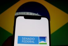 Celular com o logo do Senado Federal com a bandeira do Brasil ao fundo