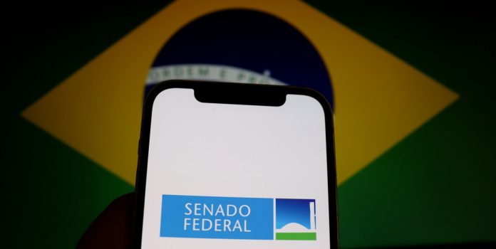 Espaço-Jurídico-Joberto-Porto-entre-regular-e-proibir-publicidade-de-apostas Celular com o logo do Senado Federal com a bandeira do Brasil ao fundo