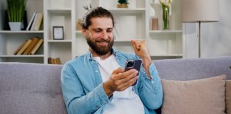 EBAC divulga pesquisa sobre comportamento do apostador durante Carnaval Homem barbudo, de cabelo longo, celebra enquanto segura o celular.