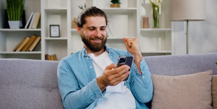 Homem-Celular Homem barbudo, de cabelo longo, celebra enquanto segura o celular.