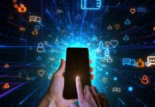 Mão segurando celular com fundo escuro cheio de símbolos relacionados a redes sociais